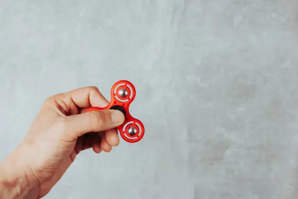 Photo of Man hand holding red plastic fidget spinner on marble background. Anti stress toy