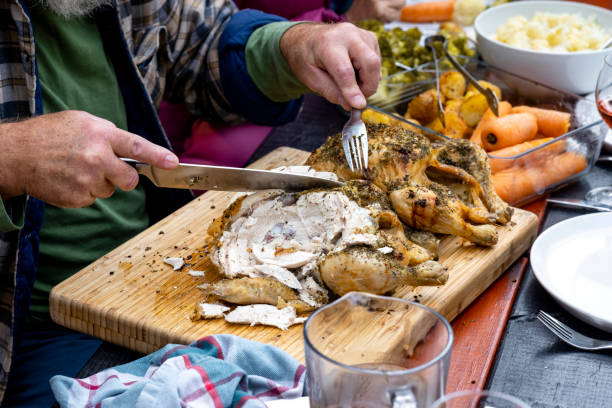 Mature gentleman carving a seasoned chicken surrounded by fresh vegetables.