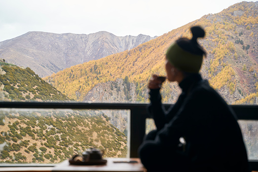 silhouette of an asian woman sitting on balcony drinking tea looking at mountains in distance