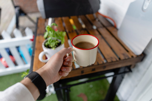 A person holding a fresh, hot, cup of coffee outdoors.