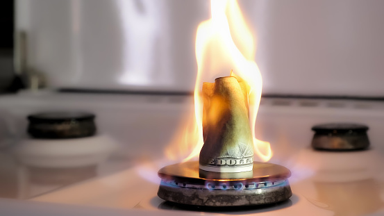 Concept of gas crisis. One hundred dollar bill is burning on a kitchen stove burner. Cash money. High prices of natural resources. Fire flame. Utility debt. Energy war. Saving home budget. Finance.