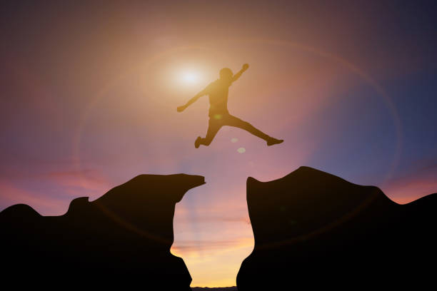 istock Silhouette Man jumping over gap between cliff with evening sunset sky background 1394383052