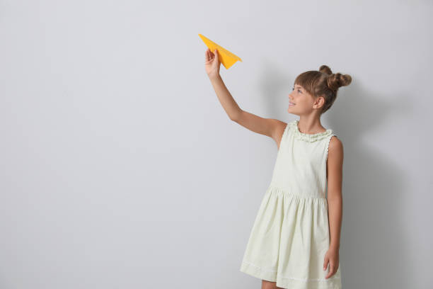 istock Cute little girl playing with paper plane on light grey background. Space for text 1394383235