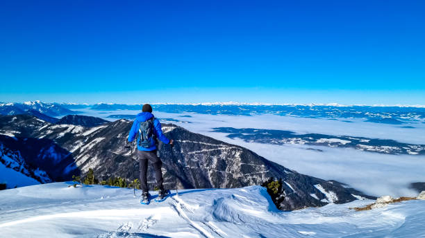 hochobir - homme sur un sentier de randonnée enneigé avec panoramique de hochobir à karawanks en carinthie, alpes autrichiennes. raquette à neige - apres ski winter hiking ski photos et images de collection
