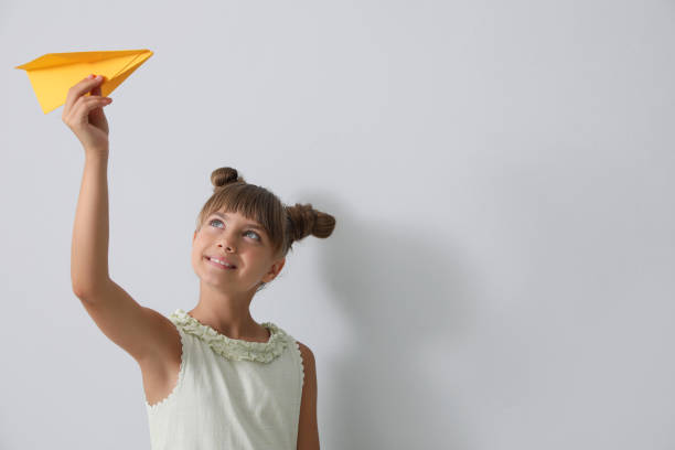 istock Cute little girl playing with paper plane on light grey background. Space for text 1394383973