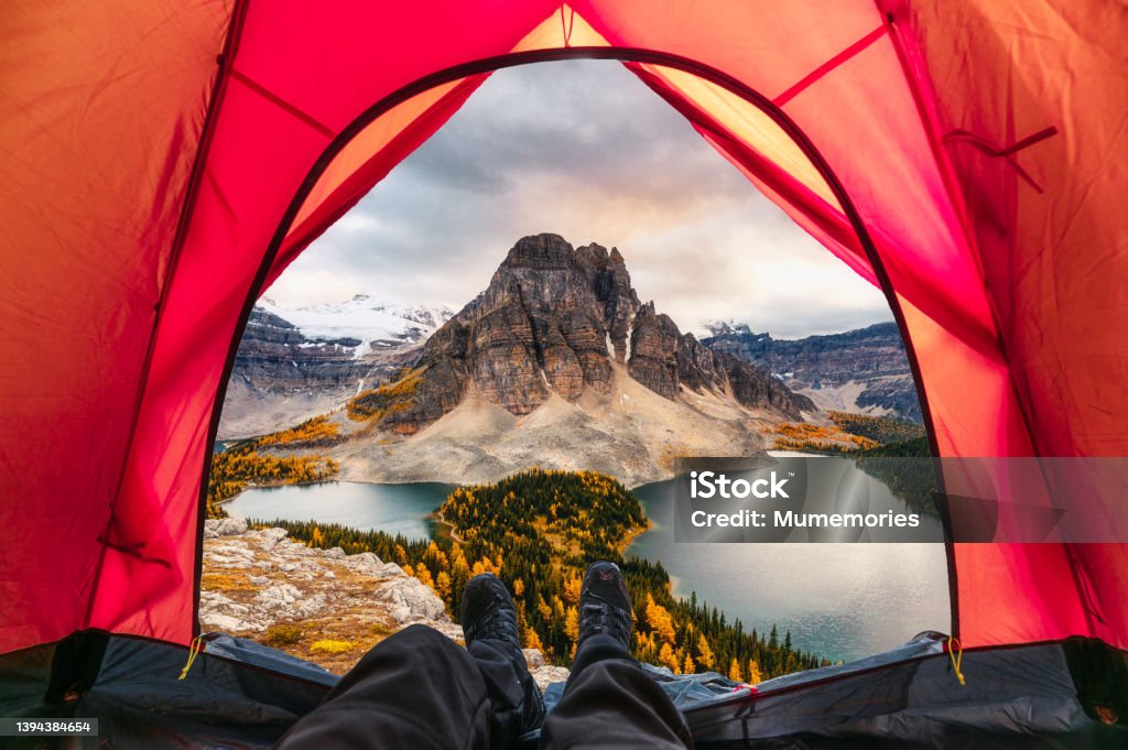 Hiker man relaxing in a tent with mount assiniboine view in autumn forest Hiker man relaxing in a tent with mount assiniboine view in autumn forest at national park Canada Stock Photo