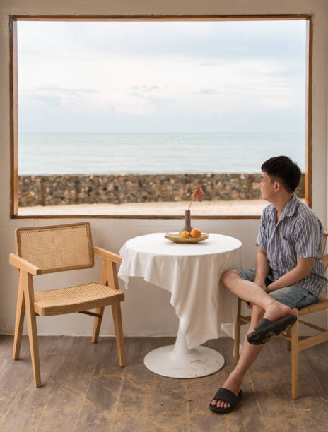 istock Young asian man sitting and looking at the beach from the window on weekend 1394384662