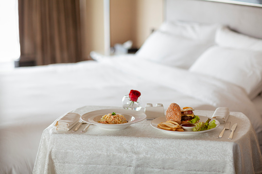 Room service food meal delivery in luxury hotel room with hamburger and spaghetti, bed and sleeping in