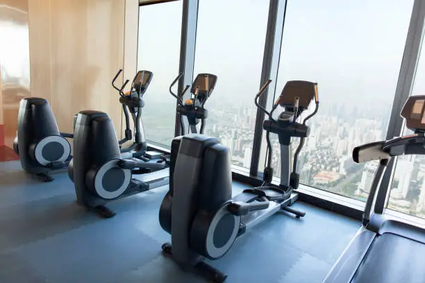Exercise elliptical machines lined up in studio with view of urban buildings in city