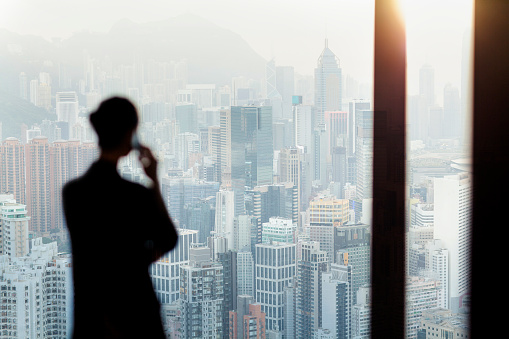 Businesswoman talking on phone from office window overlooking Hong Kong cityscape