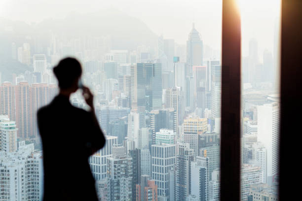 Businesswoman talking on phone from office window overlooking Hong Kong cityscape stock photo
