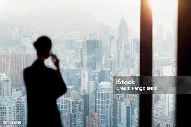 Businesswoman Talking On Phone From Office Window Overlooking Hong Kong Cityscape Stock Photo - Download Image Now