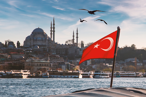 Turkish flag over Bosphorus boats, mosques, and minarets of Istanbul, Turkey.