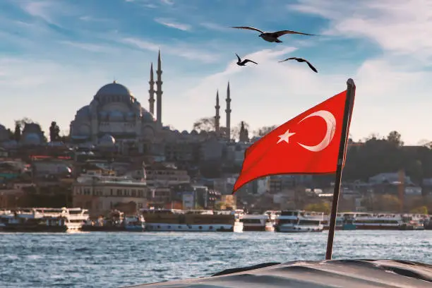 Photo of Turkish flag over Bosphorus boats, mosques, and minarets of Istanbul, Turkey.
