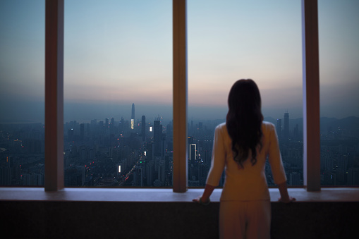 Young woman in suit looks at Shenzhen skyline from window in building