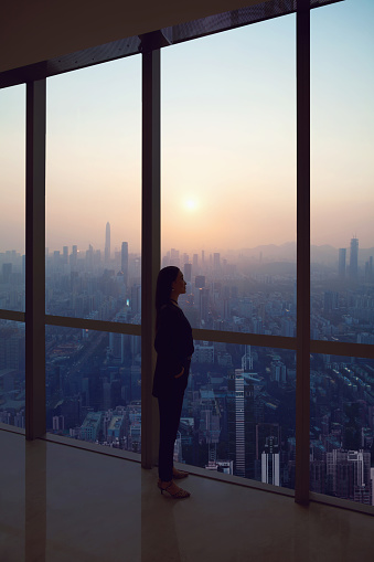 Young woman in suit looks at Shenzhen skyline from window in building, China