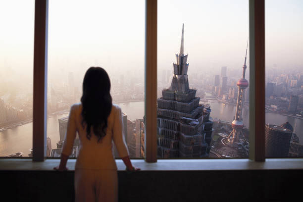 Young woman in suit looks at Shanghai skyline from window in building Young woman in suit looks at Shanghai skyline from window in building shanghai world financial center stock pictures, royalty-free photos & images