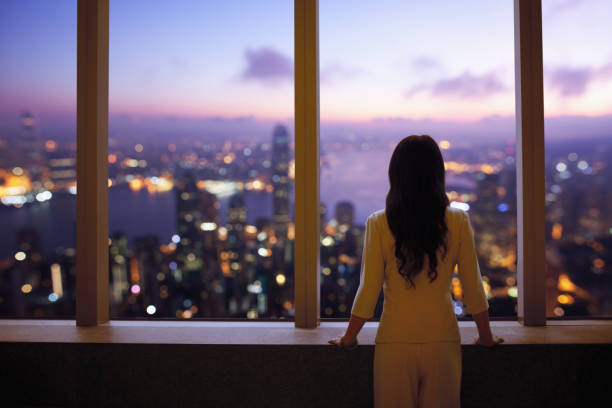 Young woman in suit looks at Hong Kong skyline from window in building stock photo