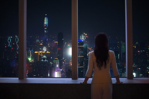 Young woman in suit looks at Shenzhen skyline from window in building