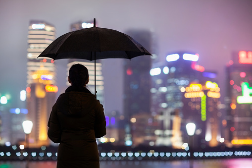 Person standing with umbrella in rain at night, Shanghai