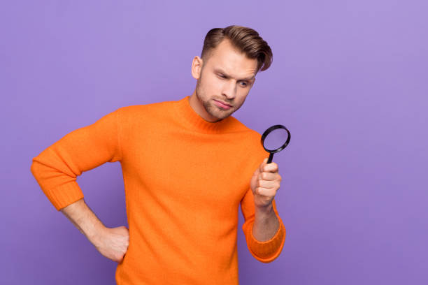 istock Photo of ponder unsure guy dressed orange pullover looking magnifier empty space isolated purple color background 1394388949