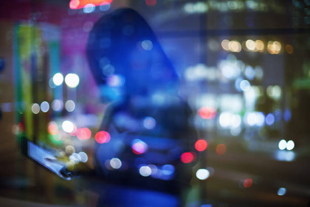 Reflection of woman in window glass at night touching a tablet computer device downtown