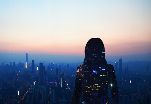Female figure in silhouette stands before futuristic urban city at dusk