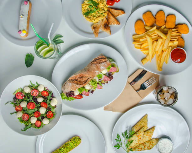 istock Breakfast with sausage and sandwich, cherry tomato and mozzarella salad, scrambled, pancakes, nagens and eclairs. Dishes on a white table with white plates. Top view 1394392806