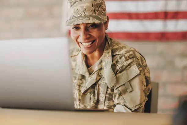 Patriotic female soldier smiling happily while video chatting with her family on a laptop. American servicewoman communicating with her loved ones while serving her country in the army.