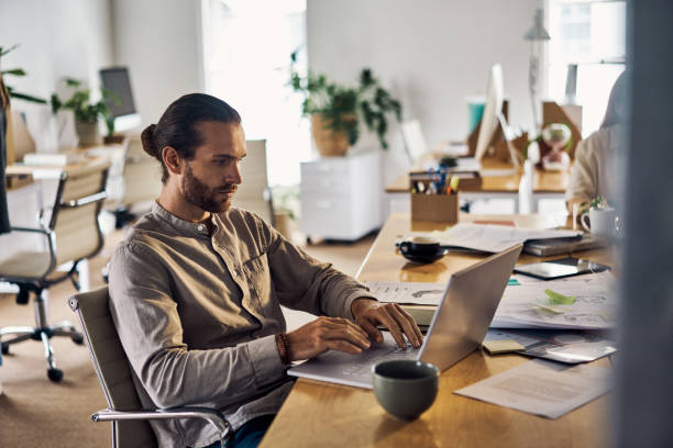 istock Young caucasian businessman using a laptop sitting at a desk at work 1394396760