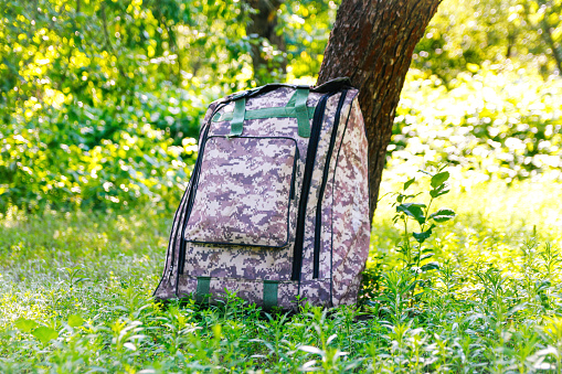 Defocus military backpack. Army bag on green grass background near tree. Military camouflage webbing material on a British army rucksack, backpack. Tourist summer hiker. Out of focus.