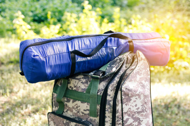 defocus military backpack and blue tent or sleeping bag. army bag on green grass background near tree. military camouflage army rucksack. tourist summer hiker. sunny. close-up. outdoor. out of focus - military canteen imagens e fotografias de stock