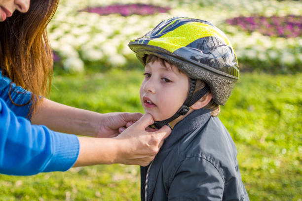 Mother helping cheerful son wearing helmet for cycle