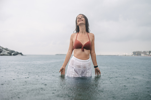 A young woman in a skirt and bikini enjoying the sea in the rain. Hot summer rain. Swimming with clothes