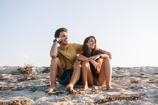 A beautiful young couple sitting at the beach and smiling