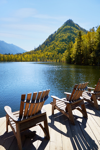 Beautiful autumn landscape. Wooden deck chairs on the lake shore. Concepts of travel and outdoor recreation.