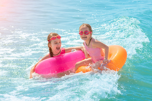 Two beautiful little girls play and have fun in sea water on the beach. Vacation or holiday concept. Children girls with inflatable swimming rings having fun in blue sea water
