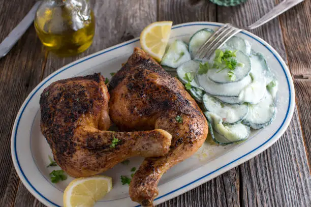 Delicious low carb or ketogenic meal with oven roasted chicken legs served with a tasty cucumber salad on wooden table background from above.