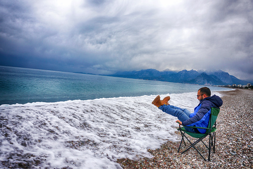 Man sitting in camping chair by the sea getting wet by waves