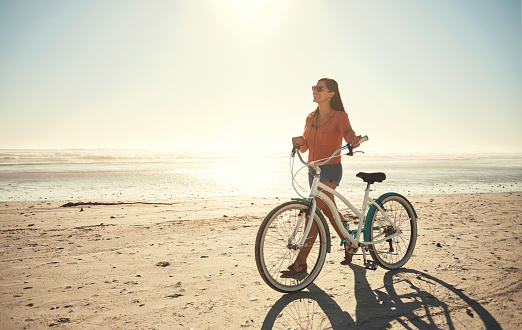 Young caucasian woman wearing glasses taking a break riding a bicycle on the beach