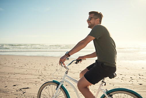 Young caucasian man riding a bicycle at the beach