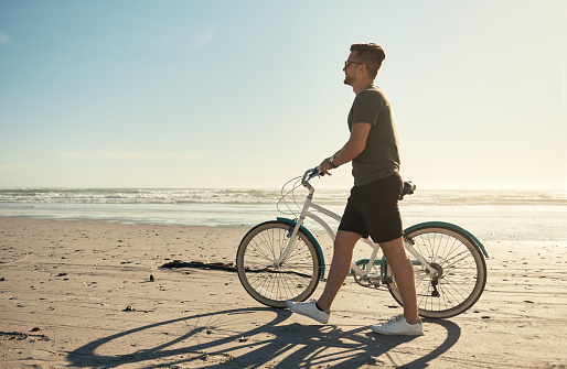 Young caucasian man enjoying a day at the beach riding a bicycle