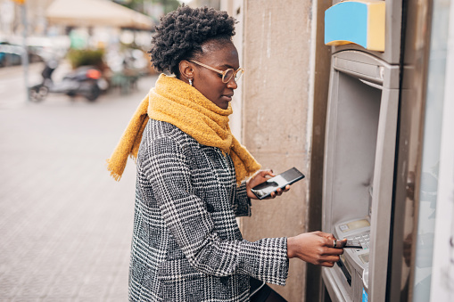 Young black women talking on the mobile phone and  using ATM and taking cash from the card