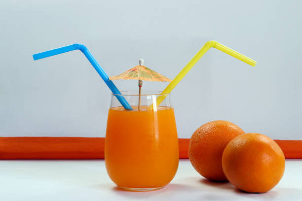 Close-up of two glasses with latte coffee and orange juice, woman drinking coffee in the background