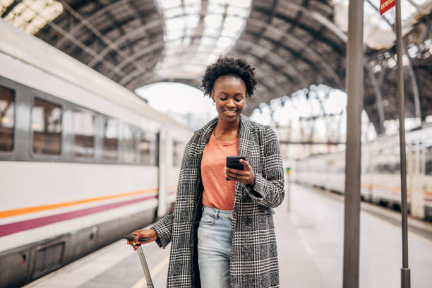 istock Young black women with suitcase on the train station using mobile phone 1394406997