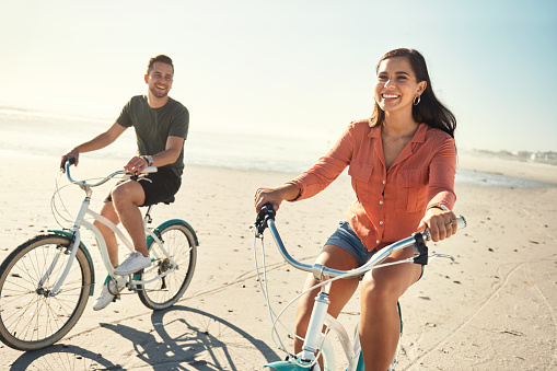 Young couple happy smiling enjoying riding bicycles together taking a break on holiday at the beach