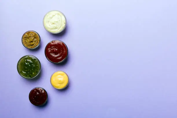 Photo of Different types of sauces in bowls on a colored Board . Top view. various sauces copy space