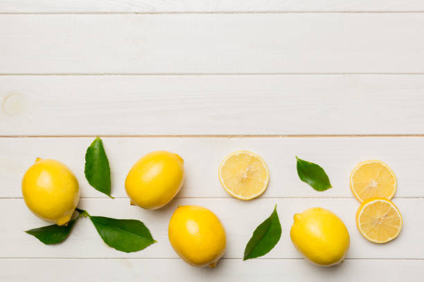 istock Many fresh ripe lemons with green leaves on colored background, top view, space for text 1394409935