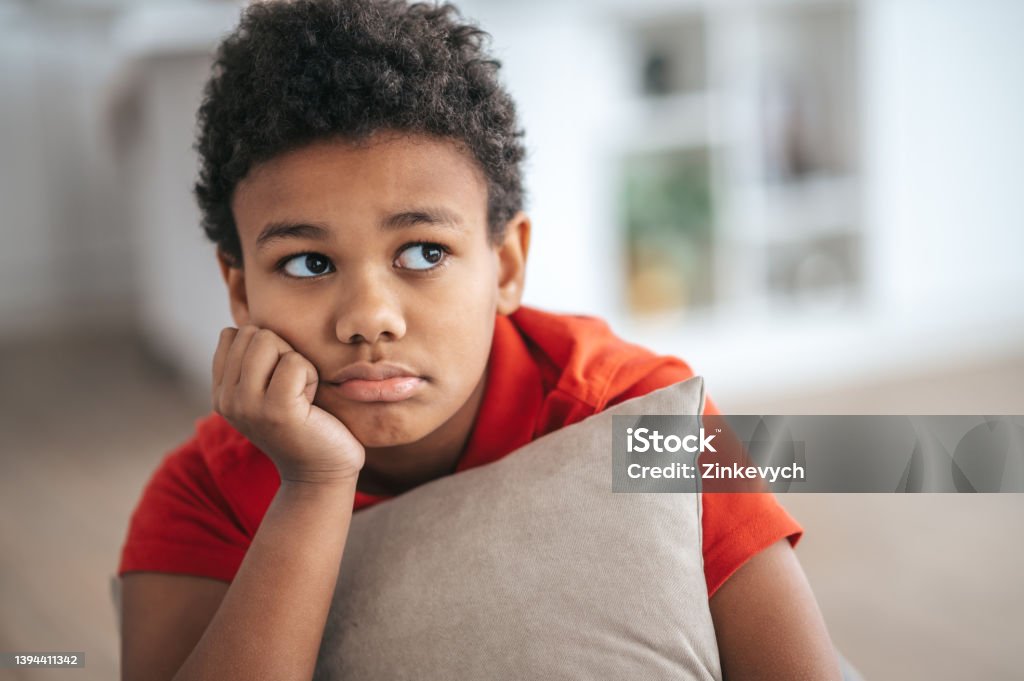 A boy with a pillow in hands looking upset Upset. A boy with a pillow in hands looking upset Sadness Stock Photo