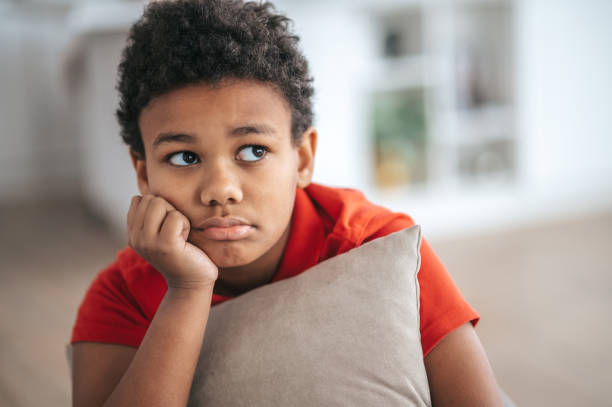 A boy with a pillow in hands looking upset stock photo